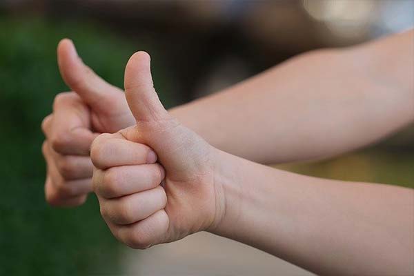 Two arms holding thumbs up after being pleased with dental service.